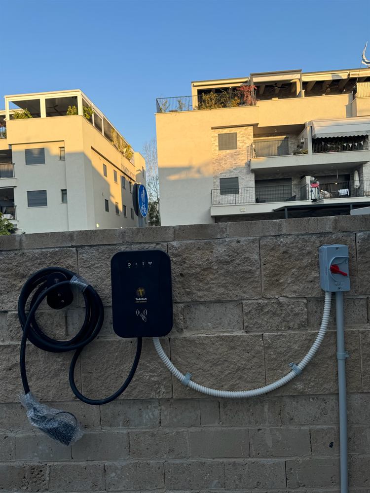 עמדת טעינה לרכב חשמלי על קיר אבן בחניית בית